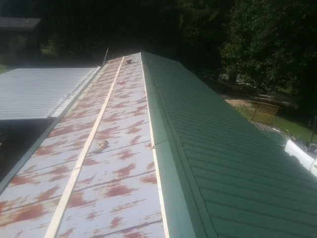 Old rusted panels beside newly installed green metal roofing — Wind Damage Roof Repair by Roofing Brothers in Carrolltown