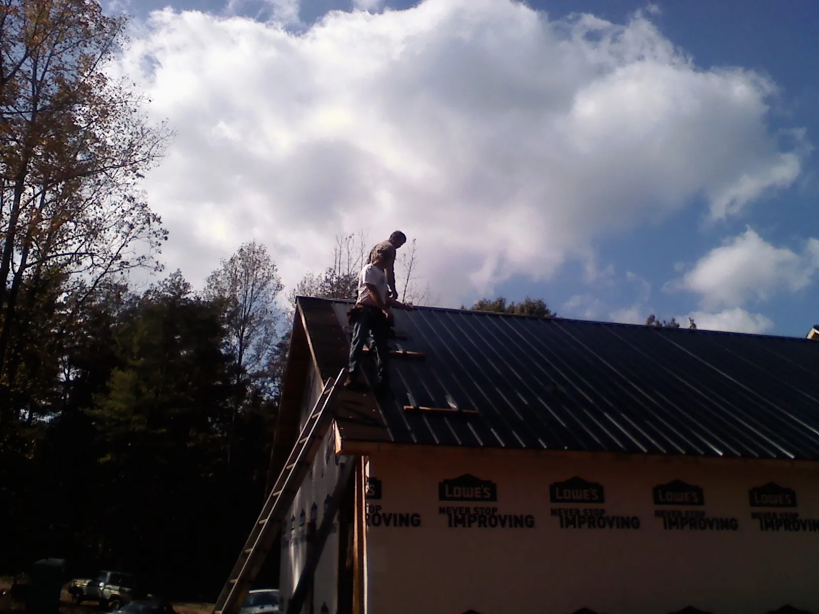 Roofer fastening dark metal panels high against a cloudy sky, from a Roof Inspection job in Carrolltown