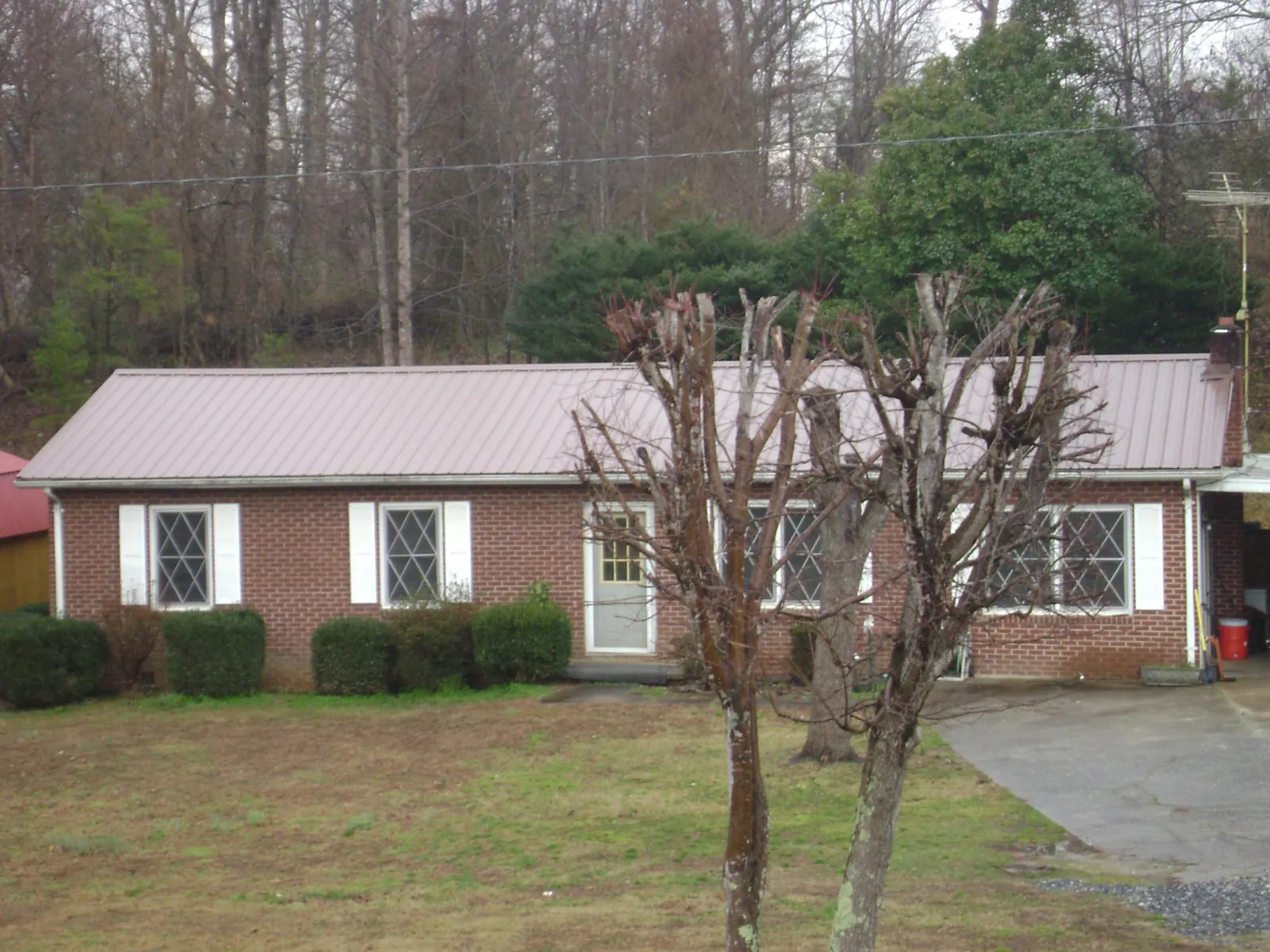 Mauve metal roof on a brick ranch home behind bare trees in Carrolltown