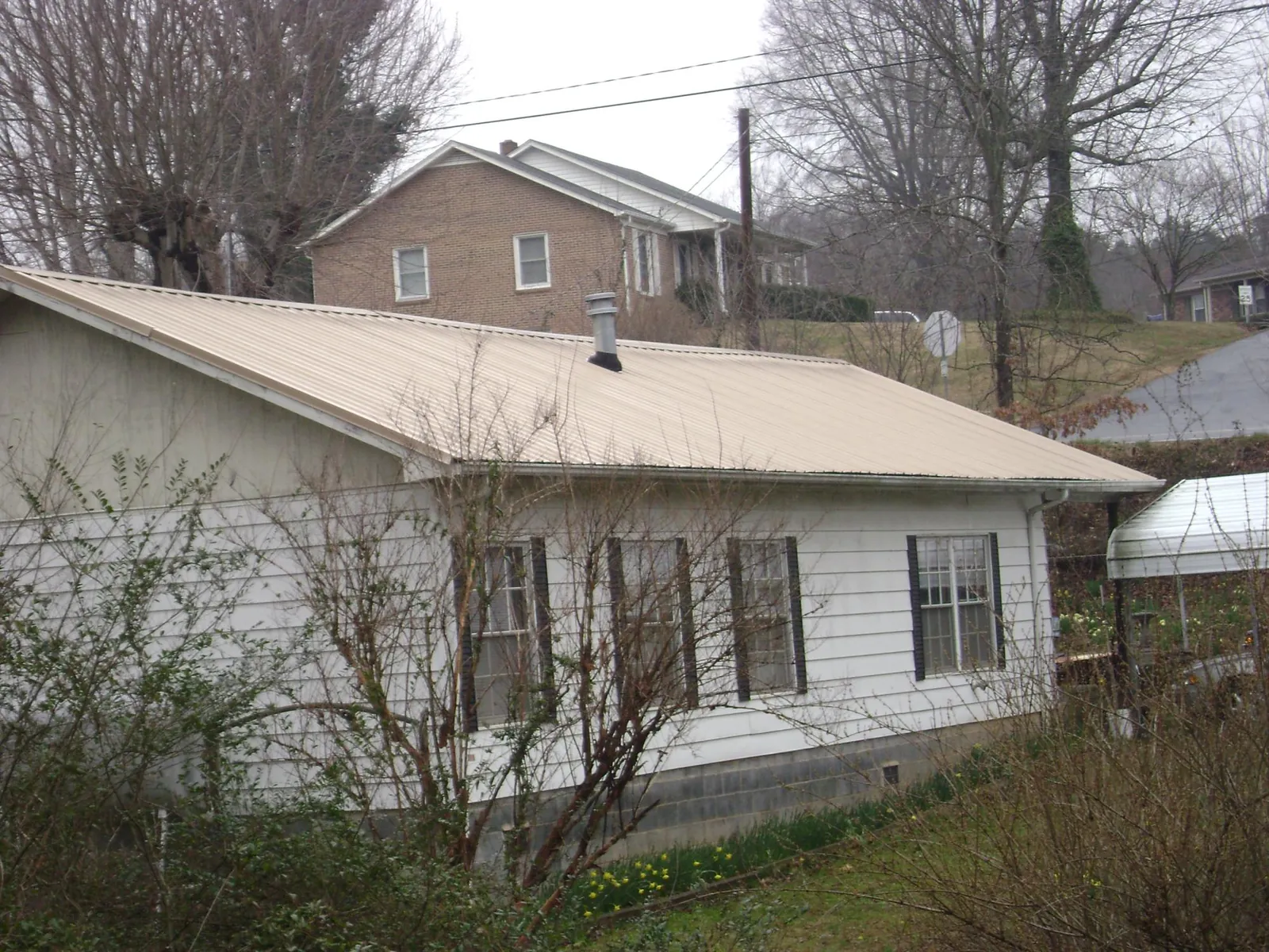 Tan metal roof on a white sided house set into a hillside — Commercial Roofing by Roofing Brothers in Carrolltown