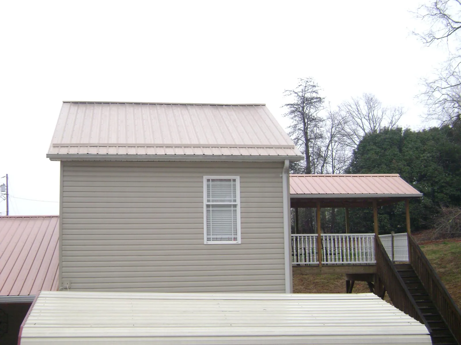 Tan metal roofs on a two story addition and attached porch, from a Roof Replacement job in Carrolltown